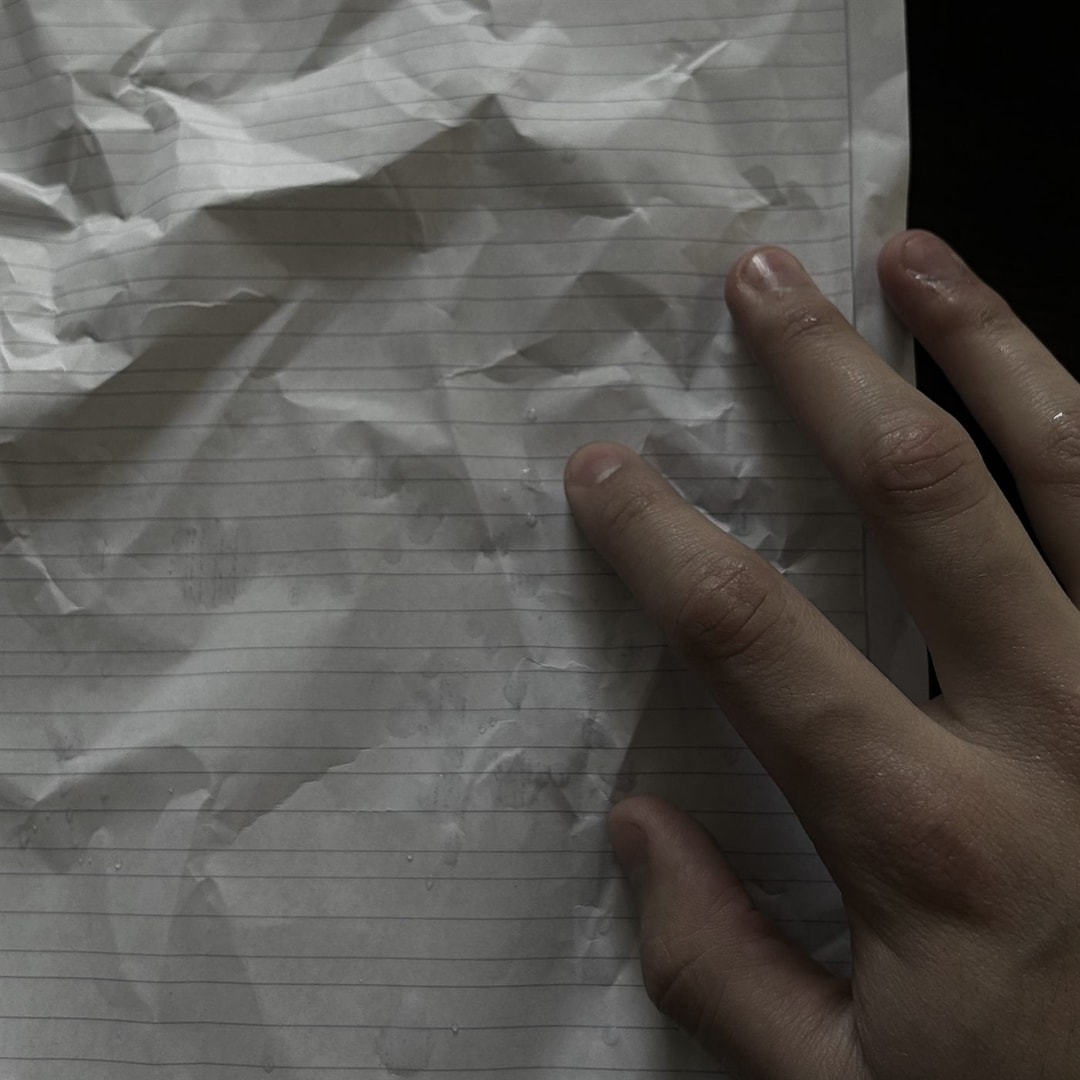 Una mano apoyada sobre una hoja de cuaderno arrugada y vuelta a estirar
